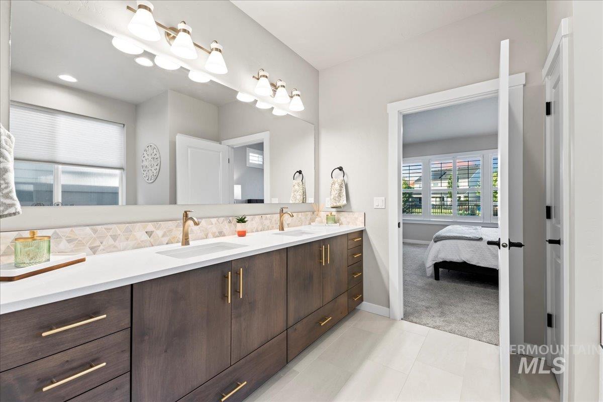 Full bathroom with double vanity, light tile patterned floors, connected bathroom, and decorative backsplash