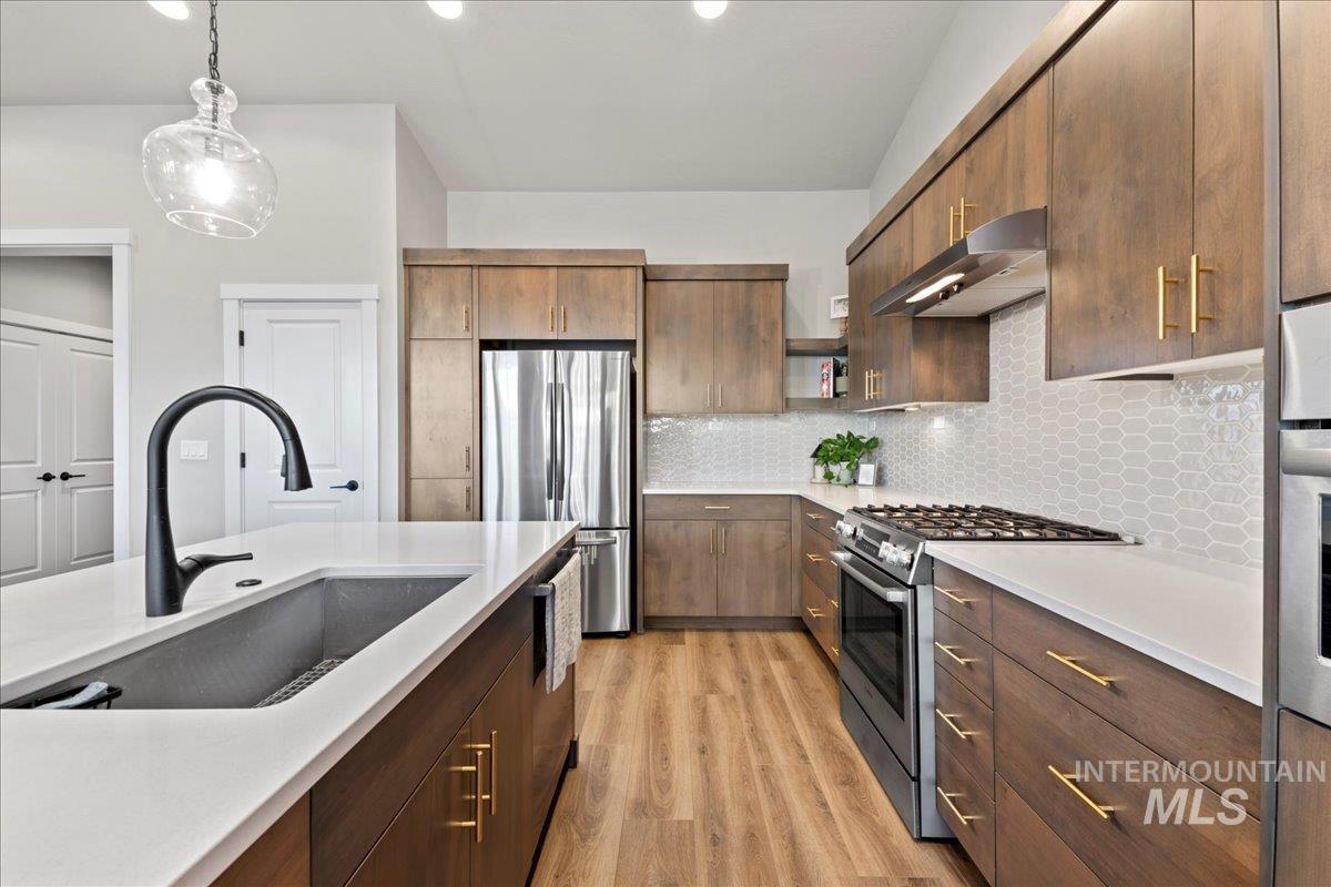 Kitchen with appliances with stainless steel finishes, hanging light fixtures, tasteful backsplash, under cabinet range hood, and light wood finished floors