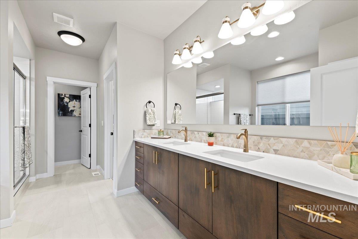 Full bath featuring tasteful backsplash, double vanity, a shower stall, light tile patterned flooring, and a walk in closet