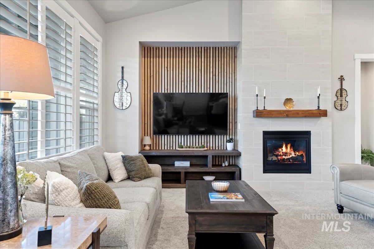 Carpeted living area featuring a tiled fireplace and lofted ceiling