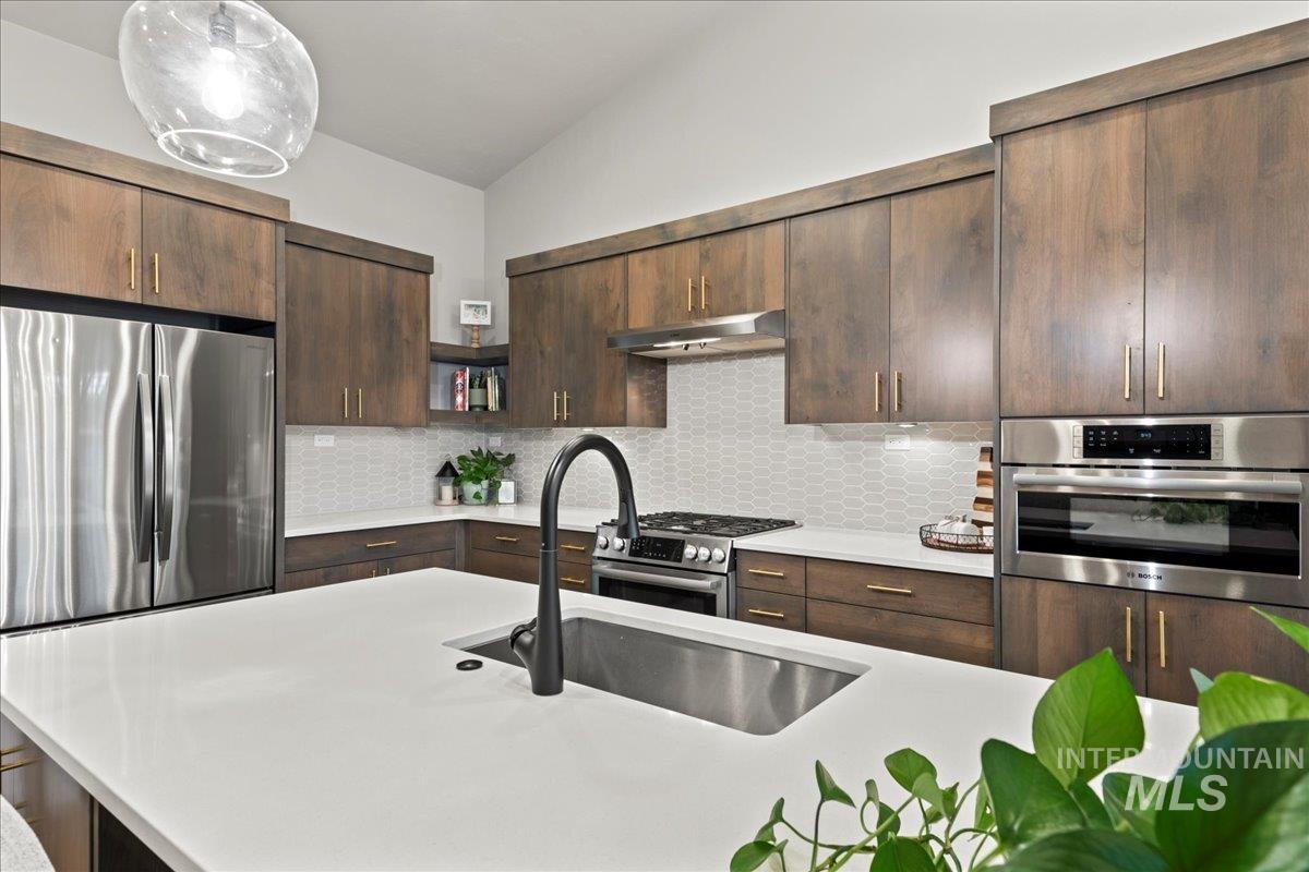 Kitchen featuring stainless steel appliances, backsplash, dark brown cabinetry, under cabinet range hood, and lofted ceiling