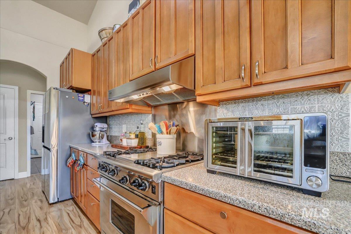 Kitchen with stainless steel appliances, under cabinet range hood, arched walkways, light wood-style floors, and decorative backsplash