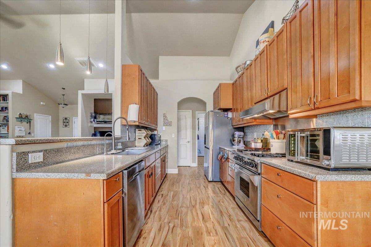 Kitchen with light wood-style flooring, arched walkways, stainless steel appliances, backsplash, and under cabinet range hood