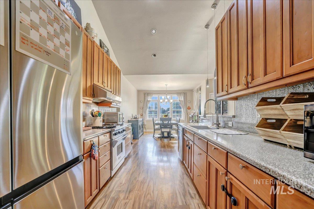 Kitchen featuring appliances with stainless steel finishes, light wood-style flooring, brown cabinets, backsplash, and a chandelier