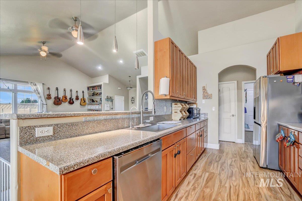 Kitchen with ceiling fan, appliances with stainless steel finishes, a peninsula, light wood-style floors, and vaulted ceiling