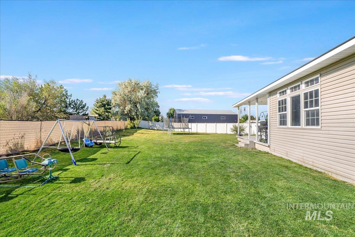 Fenced backyard featuring a trampoline and a playground