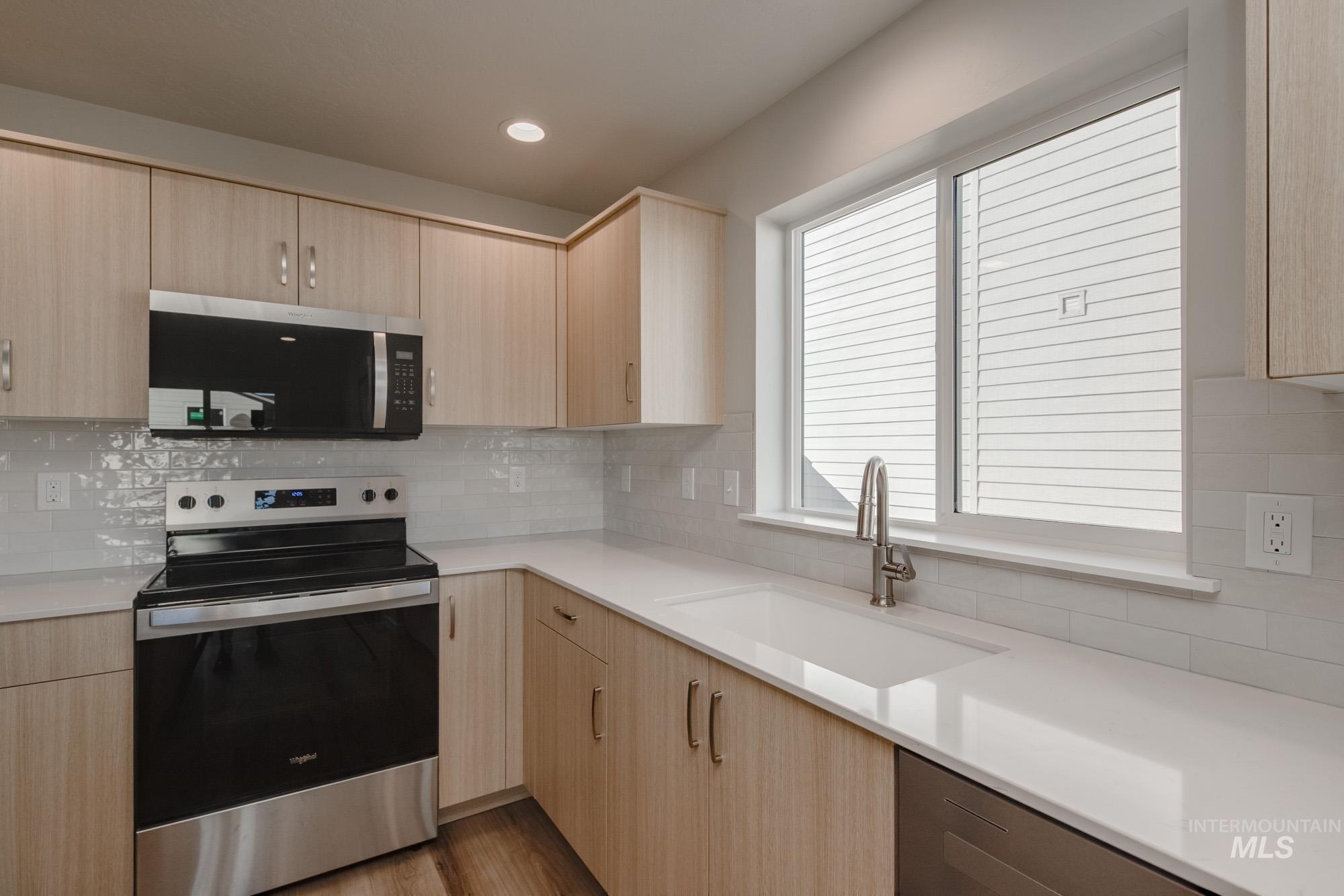 Kitchen with light brown cabinetry, stainless steel appliances, decorative backsplash, recessed lighting, and light stone counters