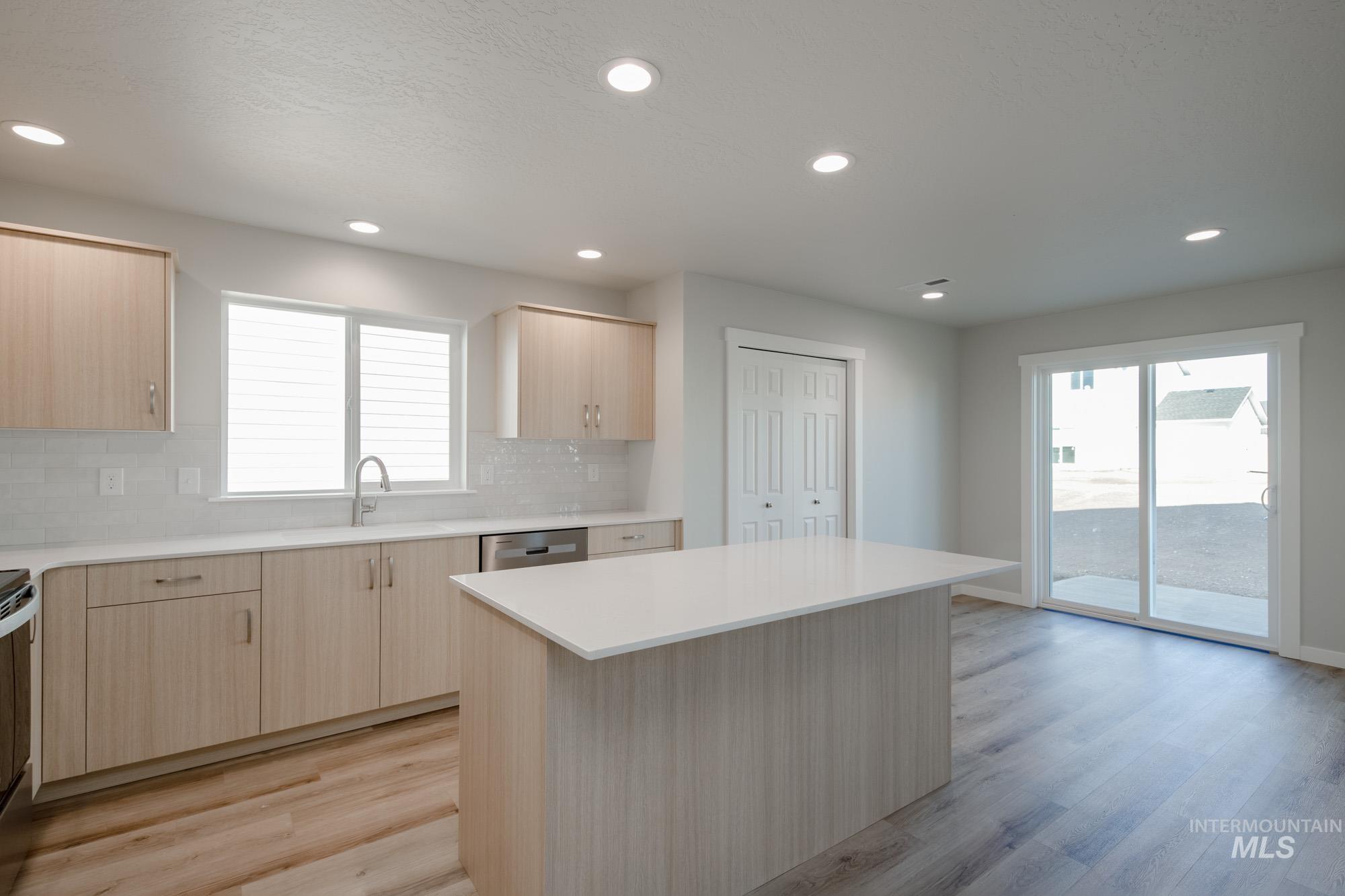 Kitchen with light brown cabinets, recessed lighting, light wood-style flooring, decorative backsplash, and a center island