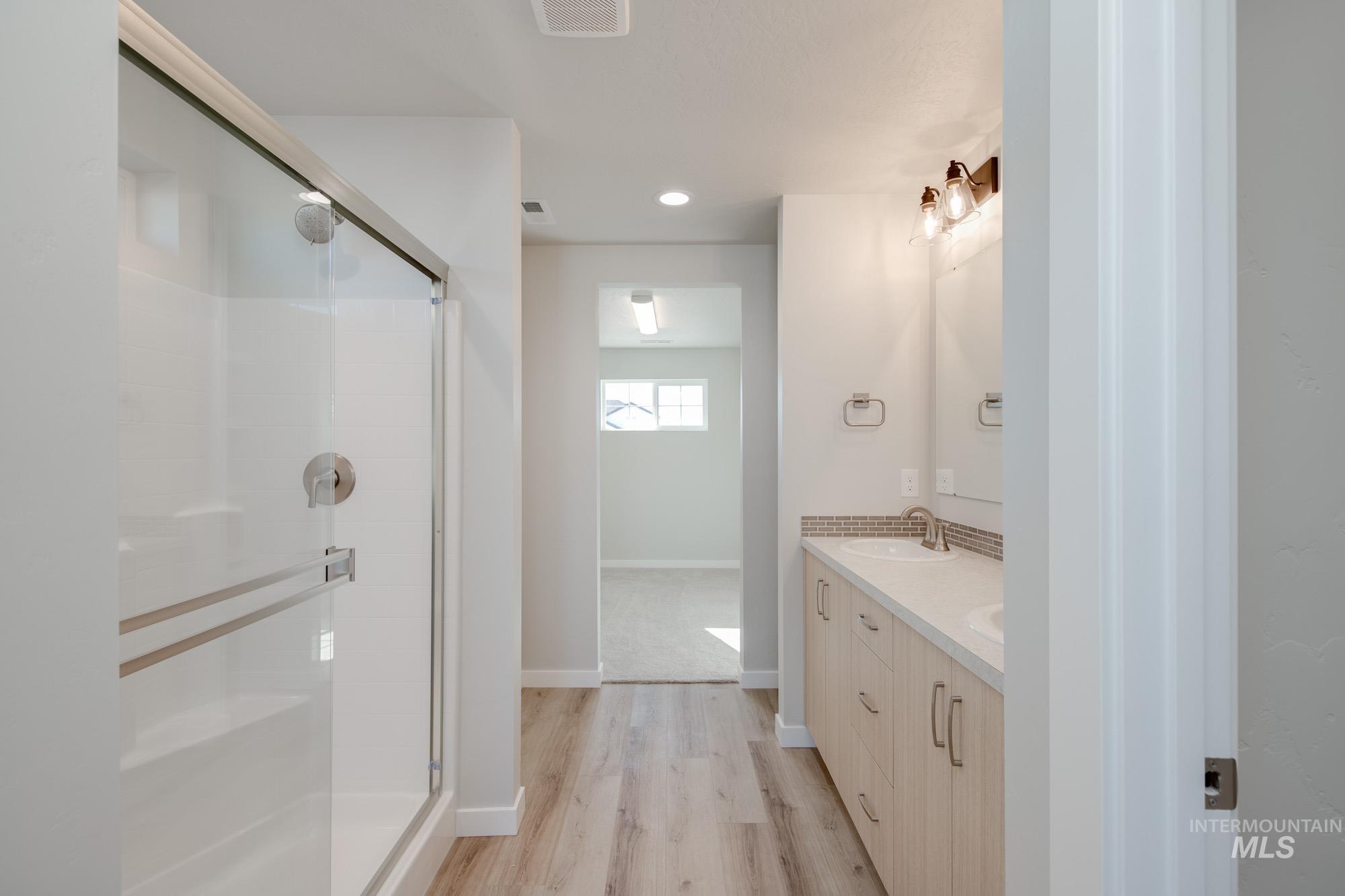 Bathroom featuring double vanity, light wood-type flooring, a stall shower, and recessed lighting