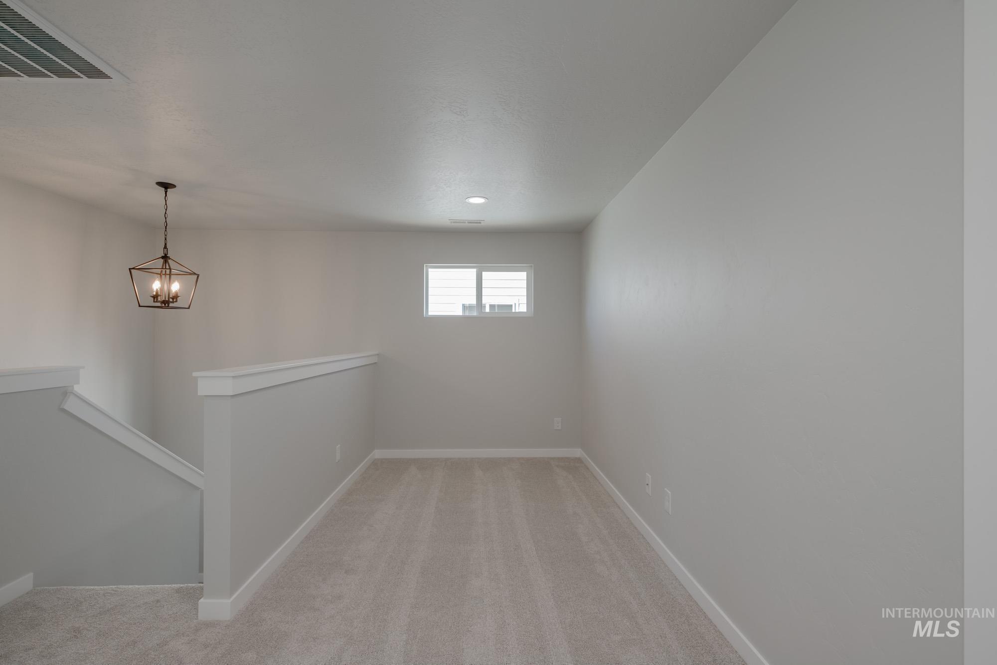Empty room with light colored carpet and a chandelier