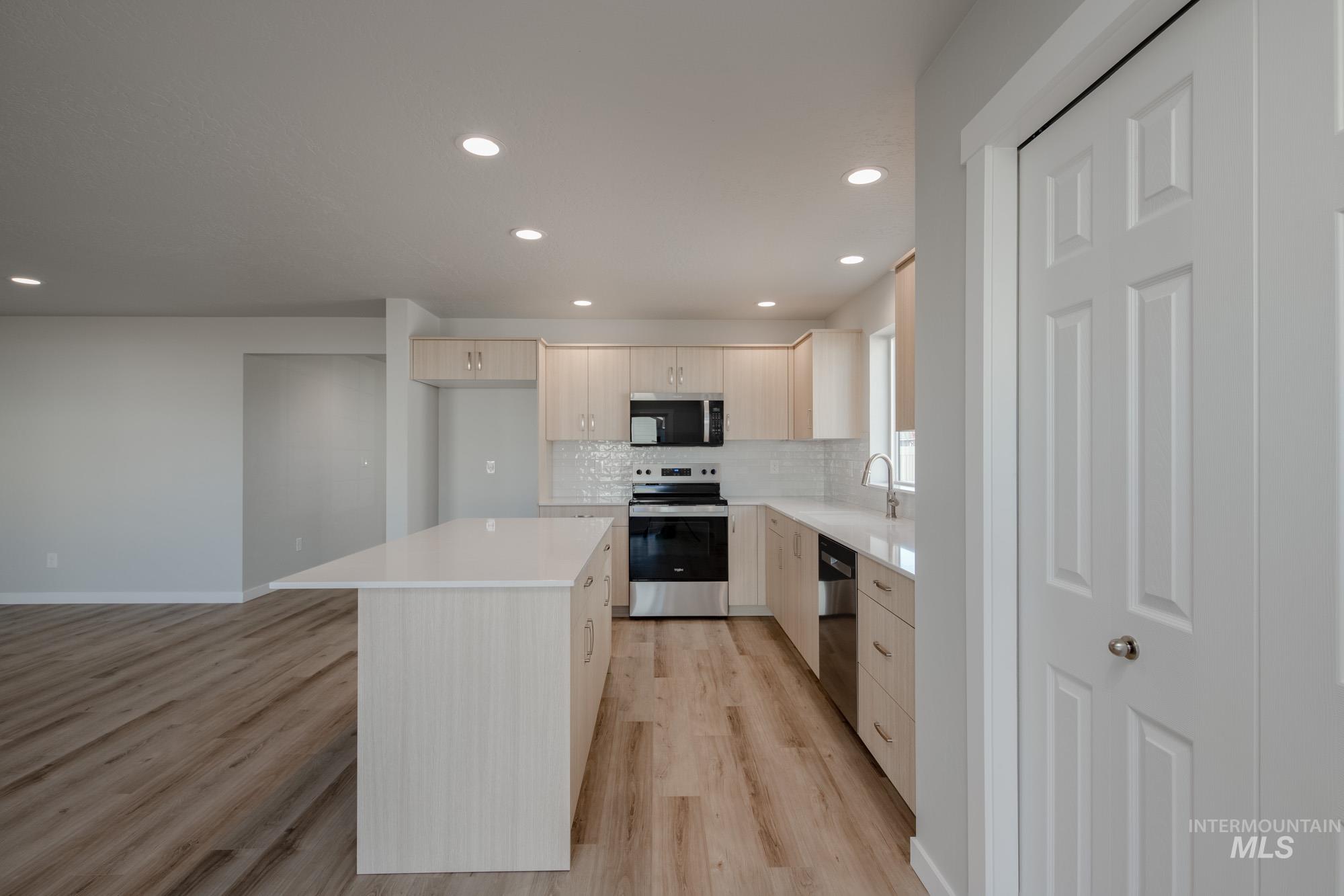 Kitchen featuring light brown cabinets, appliances with stainless steel finishes, recessed lighting, light wood-style floors, and a center island