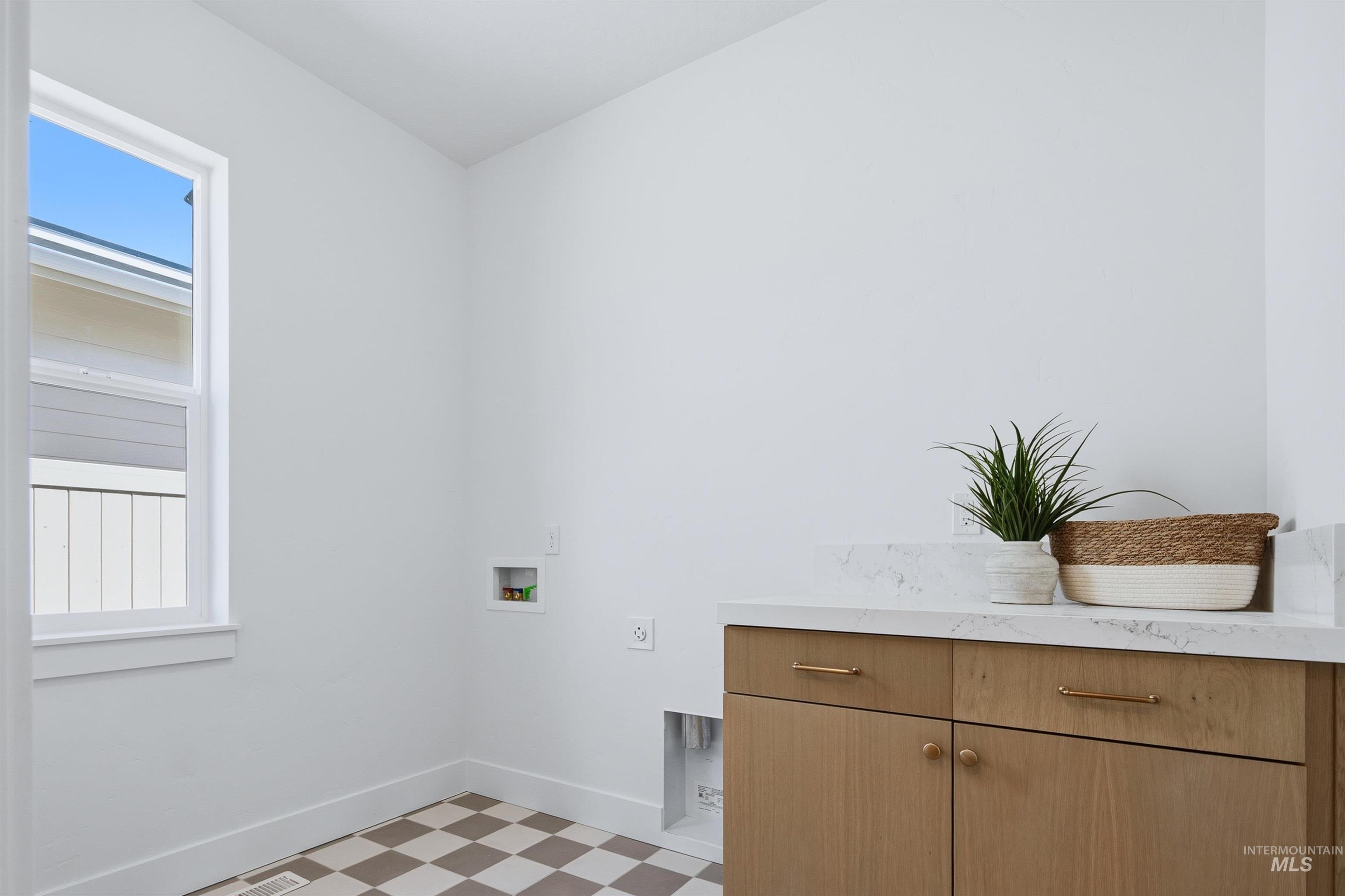 Utility room featuring a built-in wood-finish cabinet with brass hardware, a light-toned countertop, and checkered floor tiling