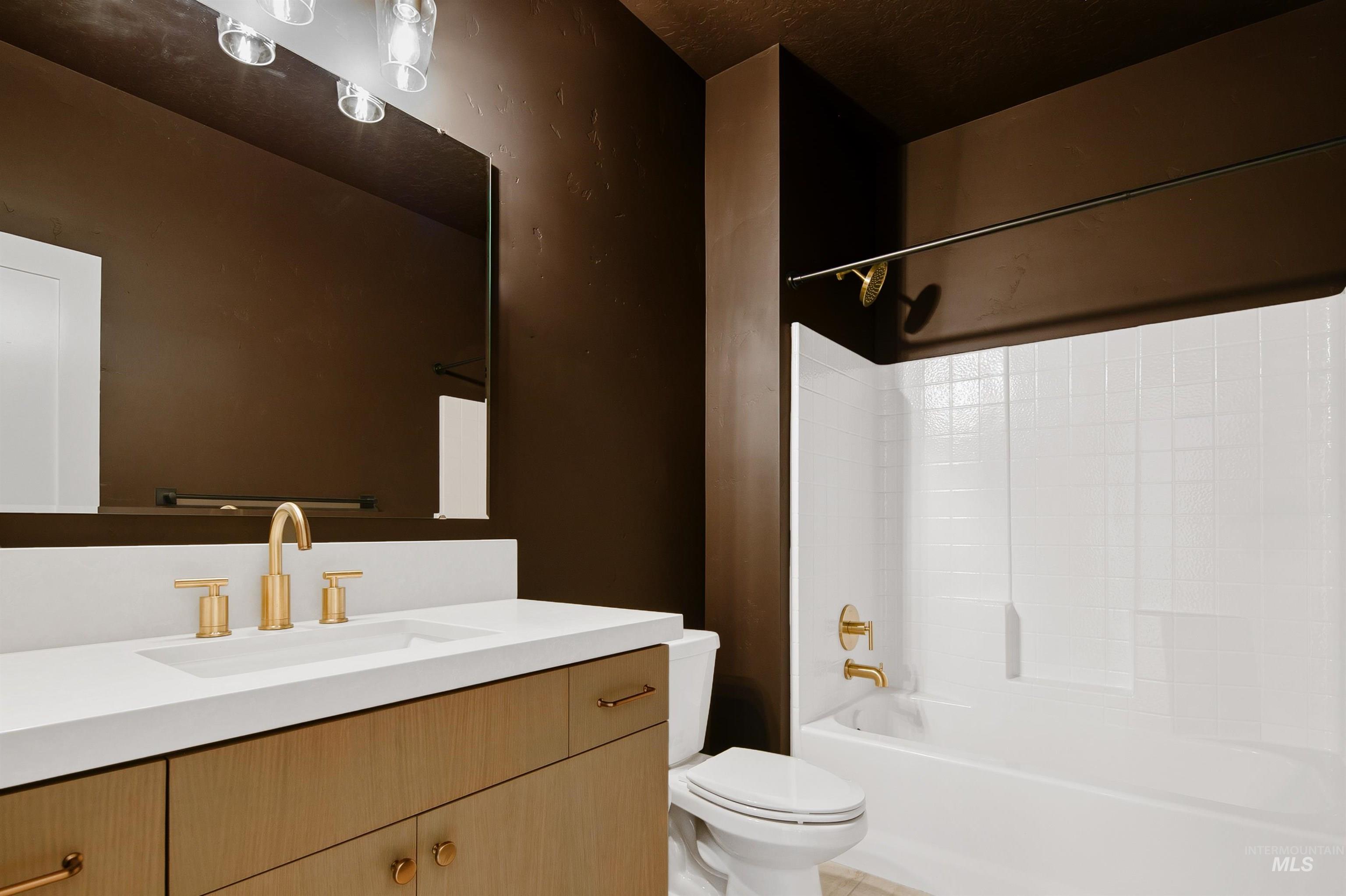 Bathroom featuring a wood-finish vanity with a white countertop and integrated sink, brushed gold fixtures, and a large mirror