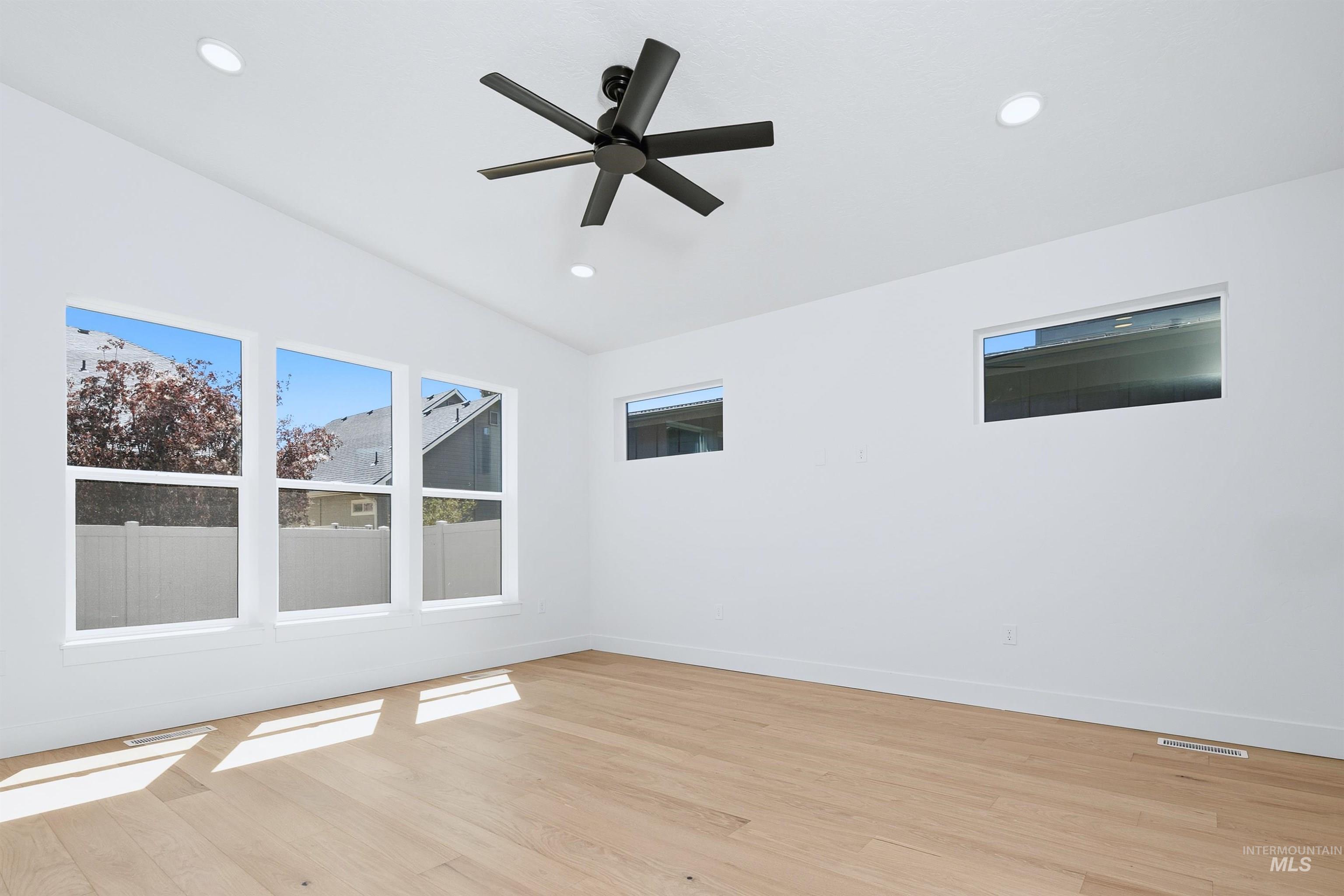 Vaulted ceiling bedroom with light wood-finish flooring, a modern black ceiling fan, recessed lighting, and multiple windows