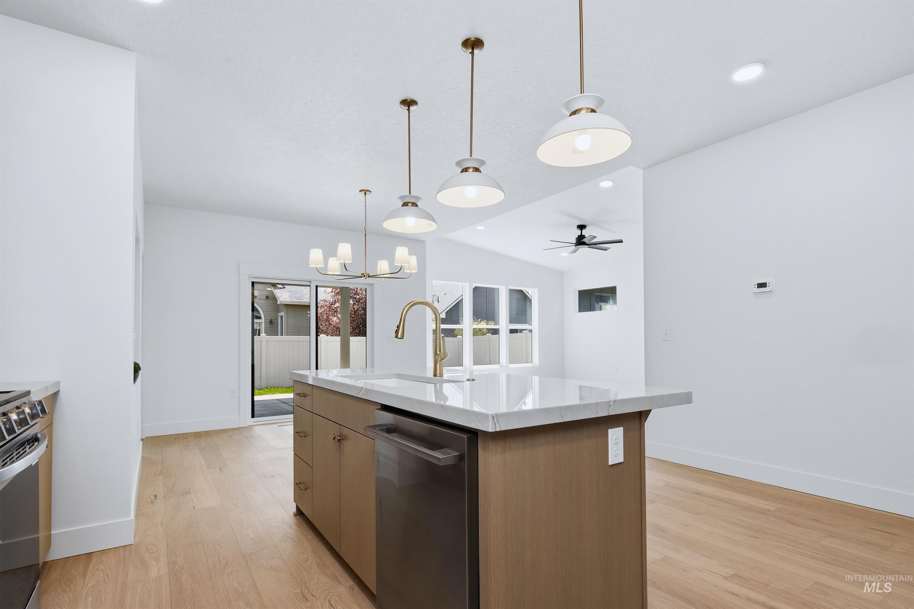 Open-concept kitchen featuring a central island with a light-toned wood-finish base, integrated stainless steel dishwasher, and a light-toned countertop