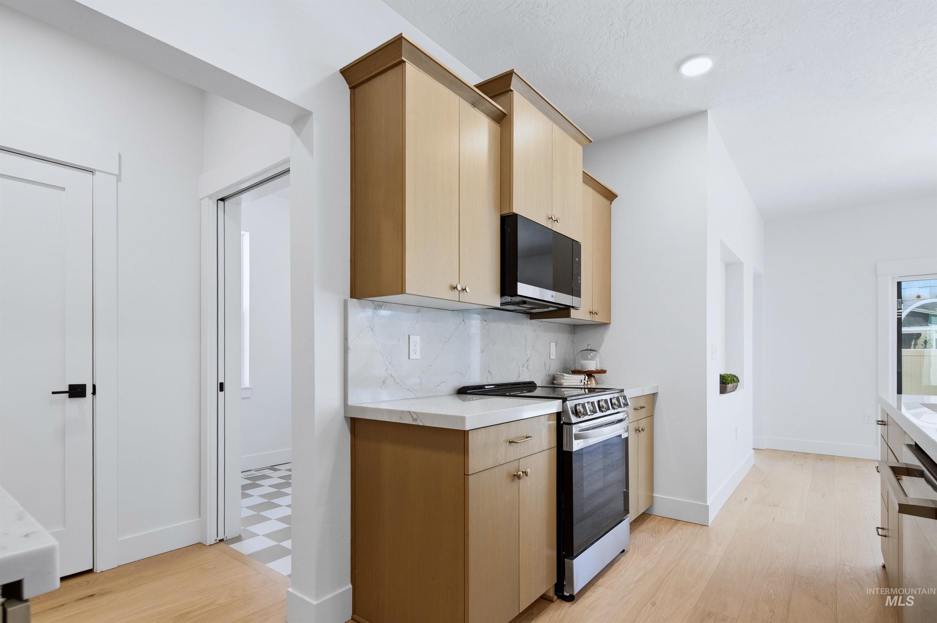 Kitchen featuring wood-finish cabinetry, stainless steel range and microwave, white countertops, and a white tile backsplash