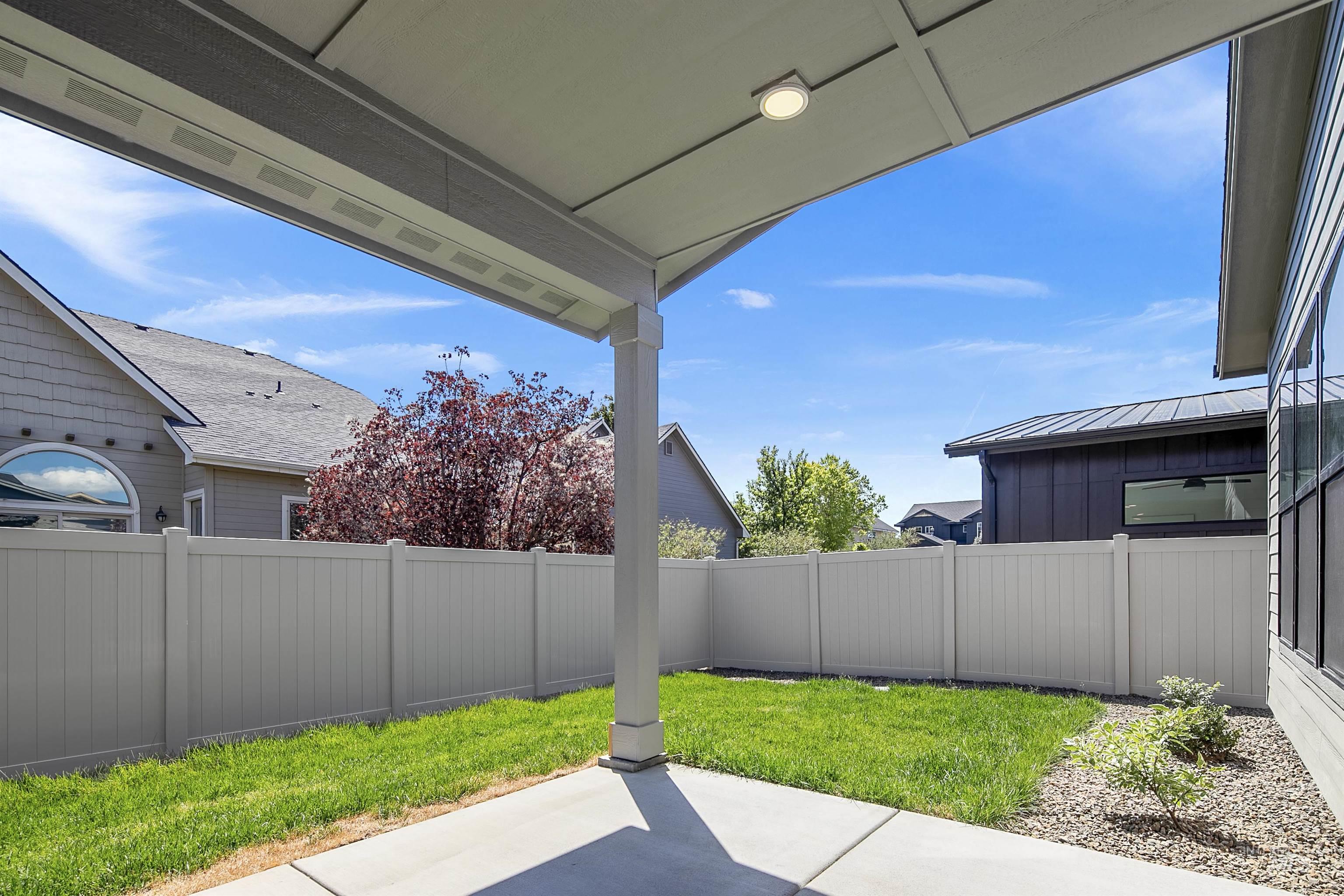 Covered patio featuring a flush-mount light fixture, concrete flooring, and a white vinyl privacy fence enclosing a small lawn area