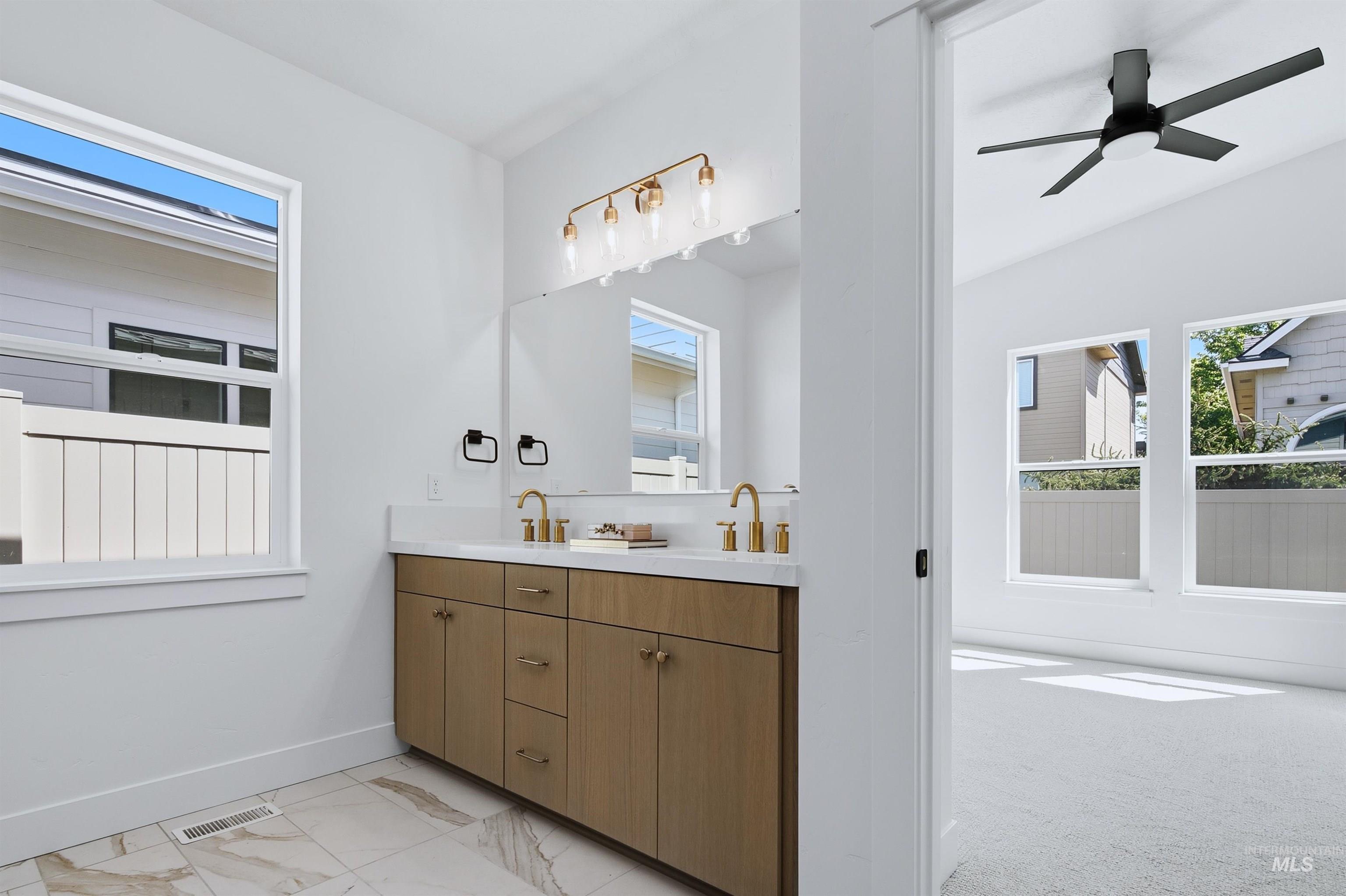 Dual vanity with wood-finish cabinetry, white countertop, and gold-finish fixtures