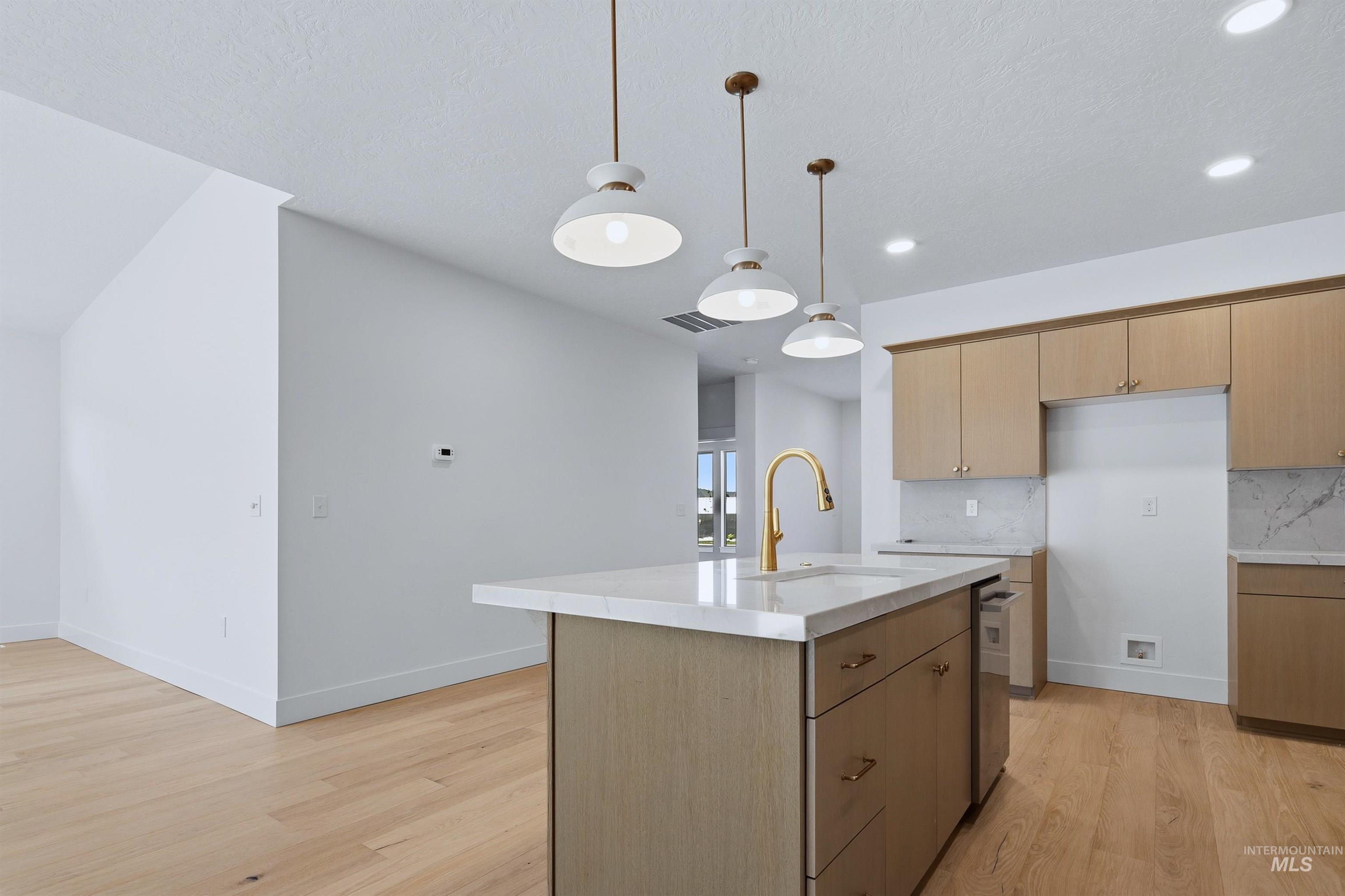 Kitchen island with light-toned wood-finish cabinetry, a light-toned countertop, and a brass-finish faucet