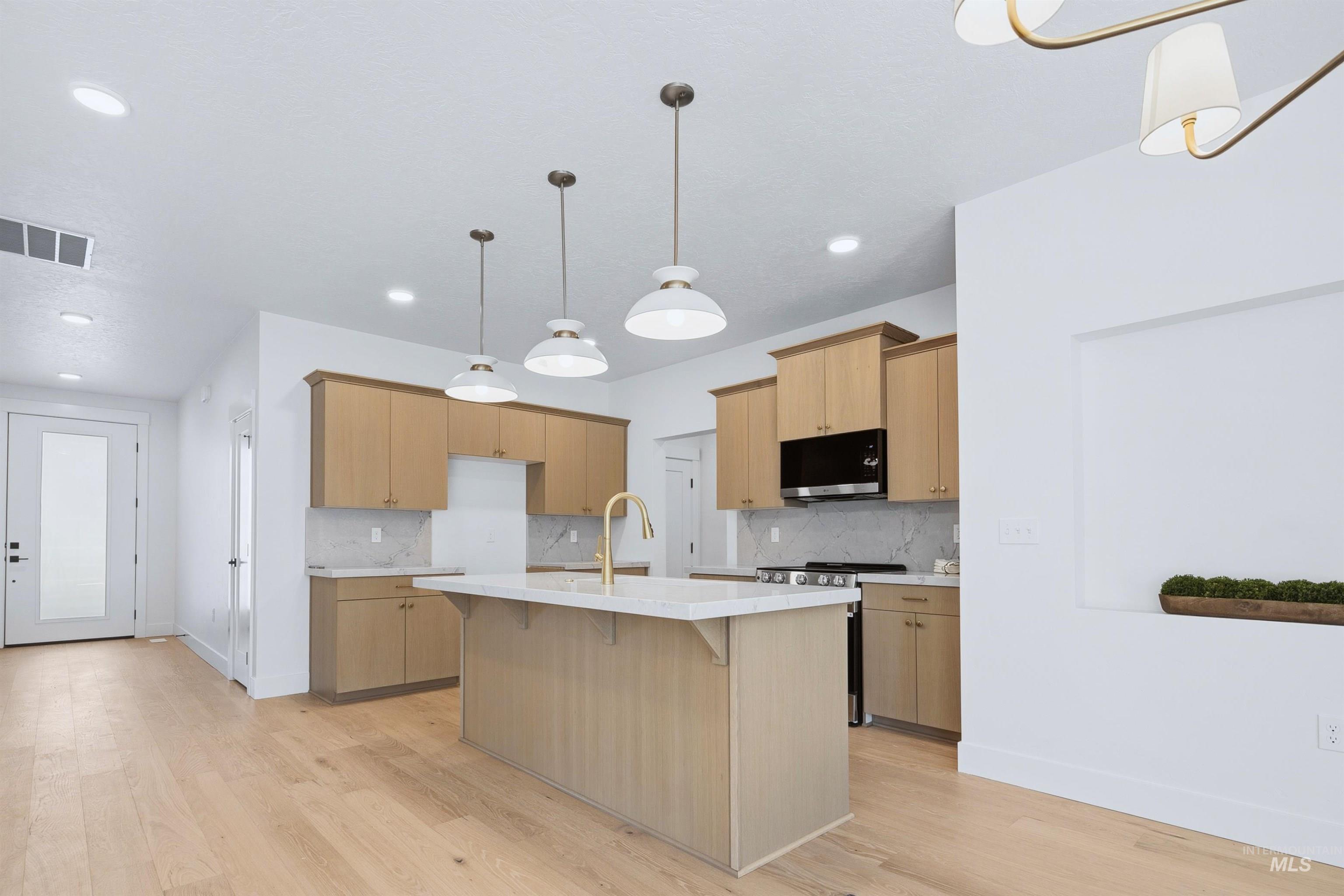 Modern kitchen featuring an island with a light-toned countertop, light wood-finish cabinetry, and a full suite of appliances including a range and range hood