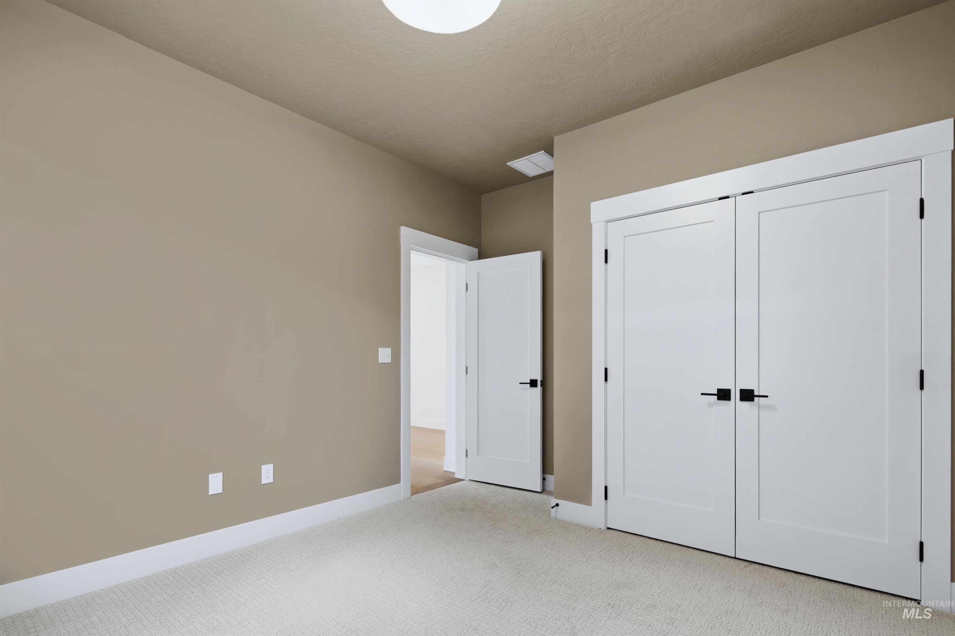Recessed ceiling light fixture, neutral-toned walls, white trim, white paneled doors with black hardware, and carpeted flooring