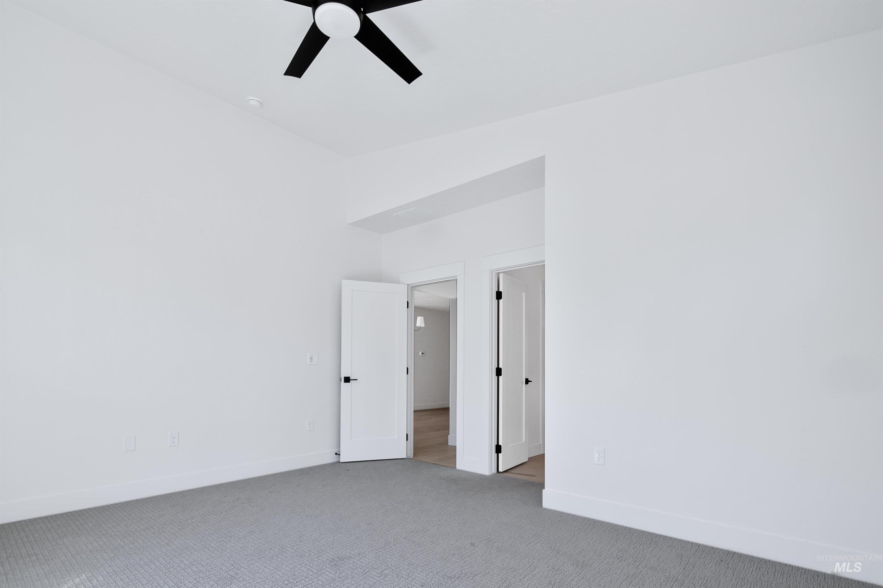 Spacious room featuring light gray carpeting, white walls, and a contemporary black ceiling fan