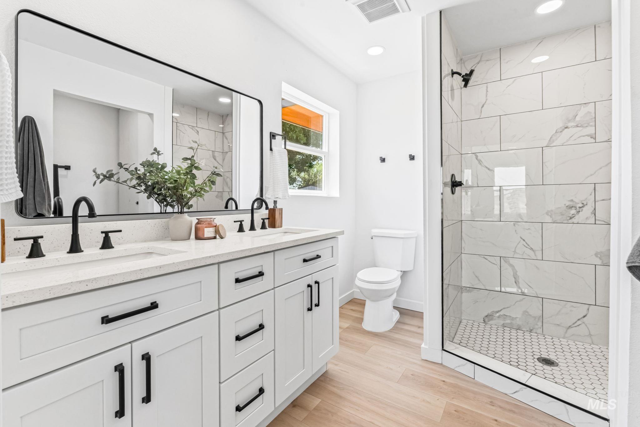 Full bathroom with double vanity, a marble finish shower, light wood-style flooring, and recessed lighting