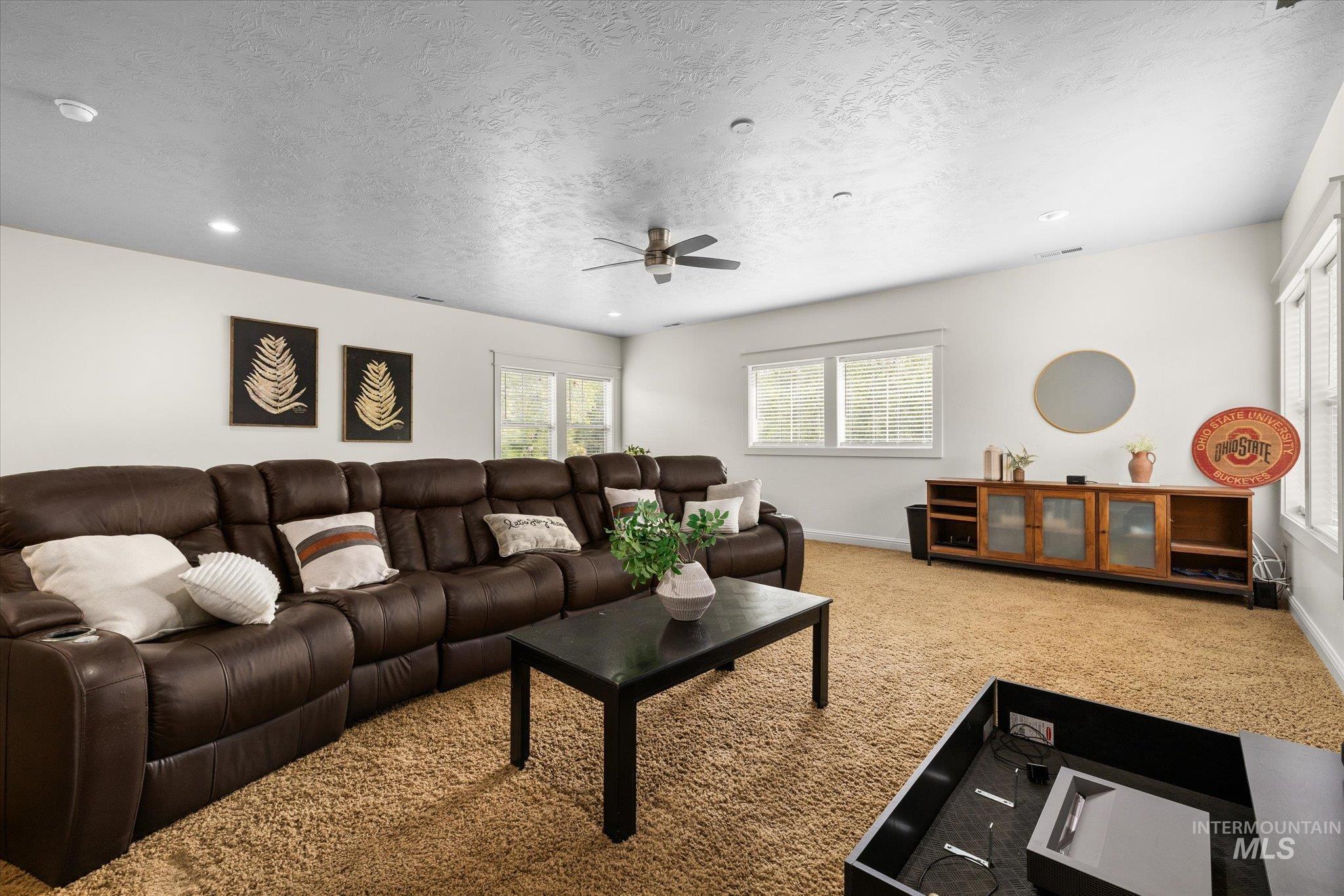Living room with light carpet, a ceiling fan, a textured ceiling, and recessed lighting