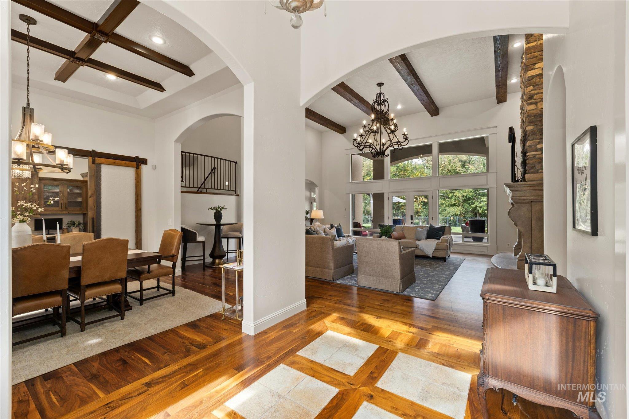 Living room with a chandelier, beamed ceiling, wood finished floors, a towering ceiling, and a barn door