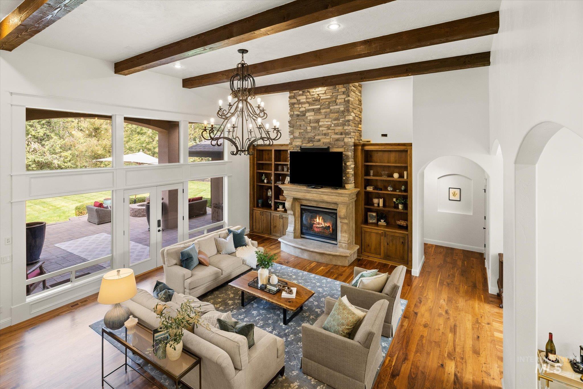 Living room with wood finished floors, a fireplace, beam ceiling, a chandelier, and a high ceiling