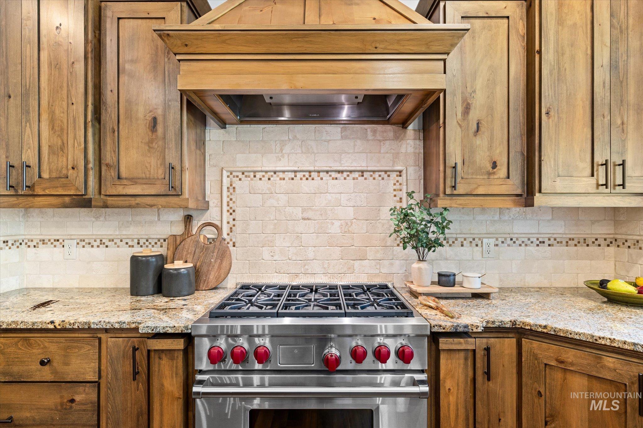 Kitchen featuring custom exhaust hood, luxury stove, decorative backsplash, and light stone countertops