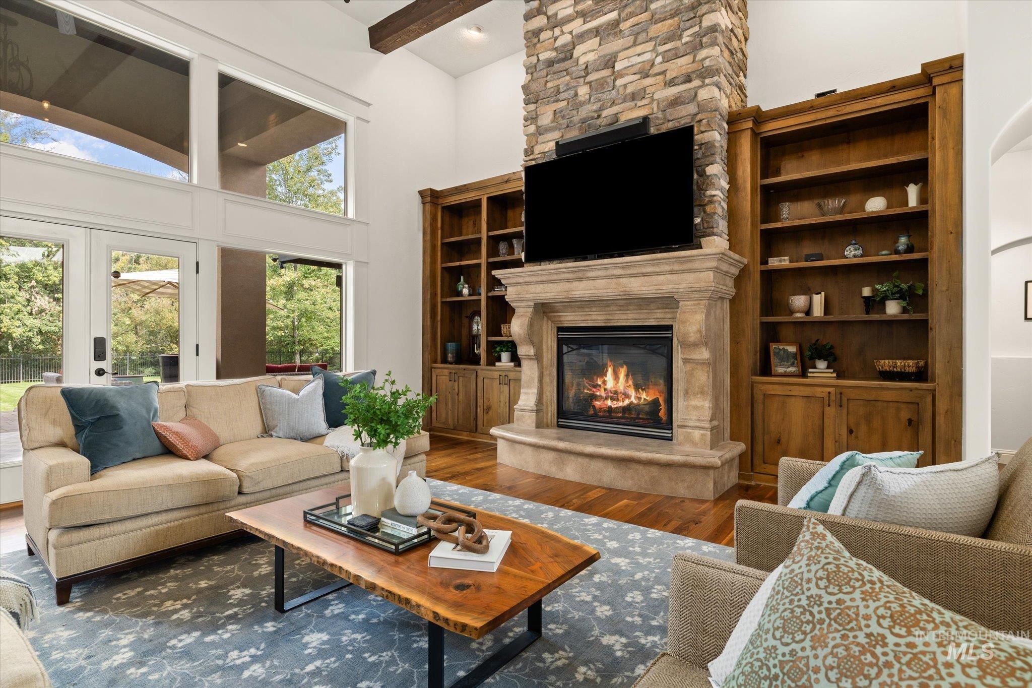 Living room with wood finished floors, a towering ceiling, a fireplace, french doors, and beam ceiling