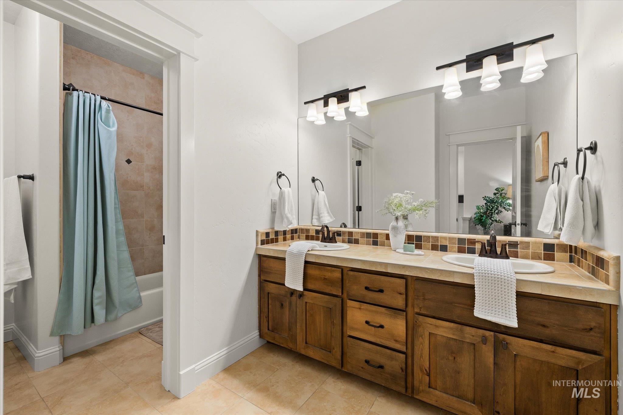Bathroom featuring shower / bath combo with shower curtain, double vanity, decorative backsplash, and light tile patterned floors