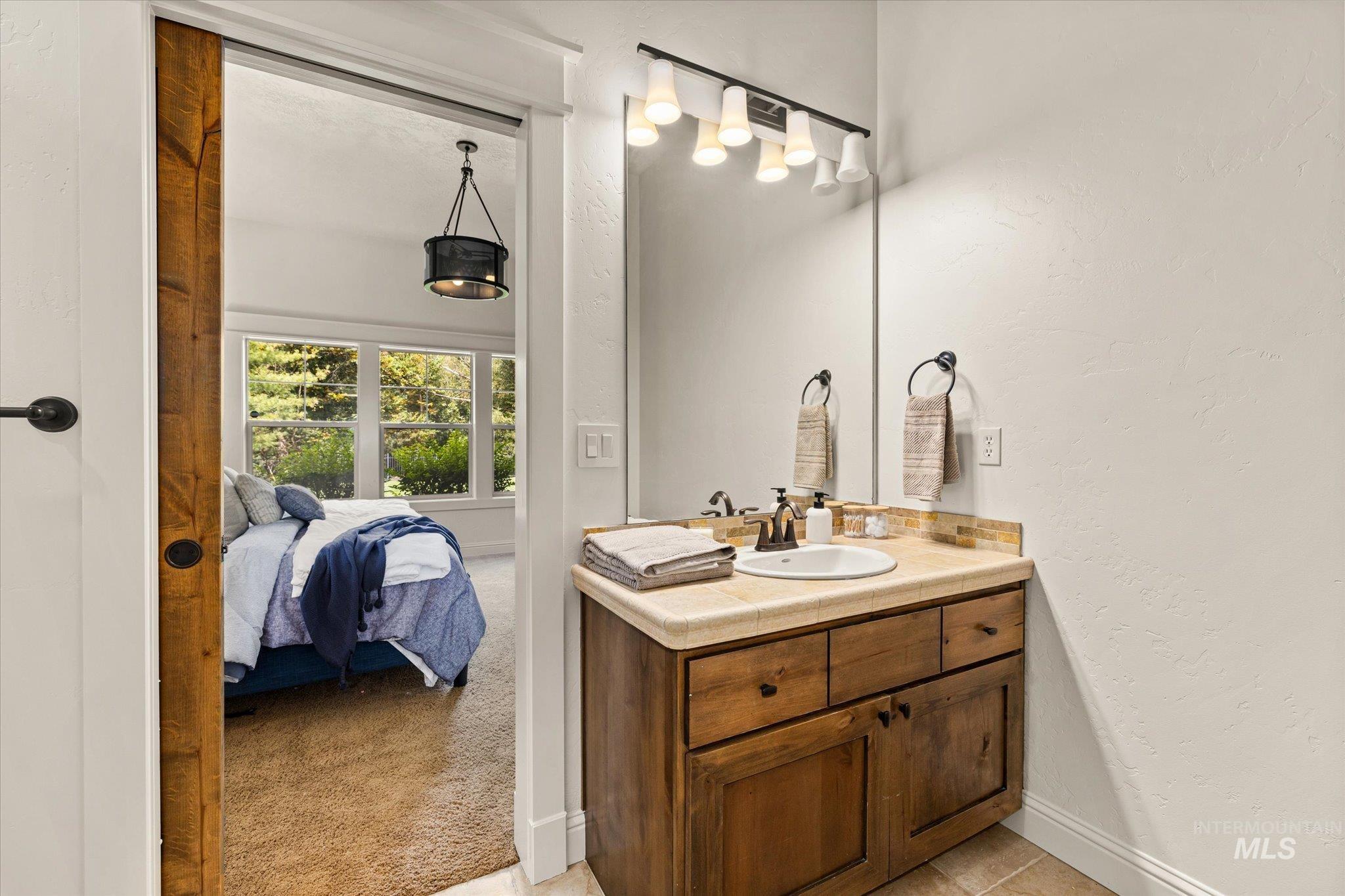 Ensuite bathroom featuring vanity, a textured wall, and light tile patterned floors