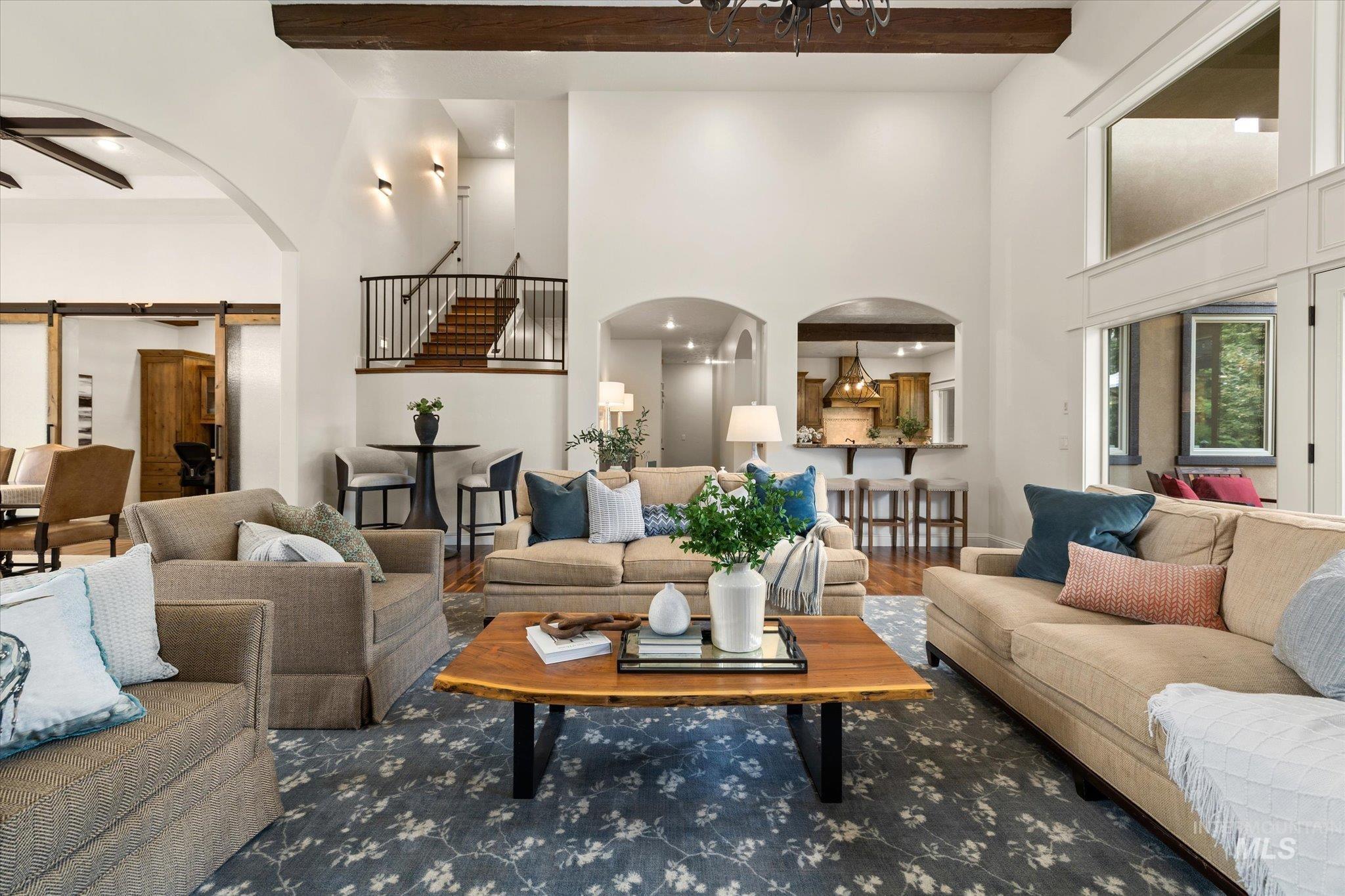 Living area with arched walkways, beamed ceiling, a barn door, wood finished floors, and stairway