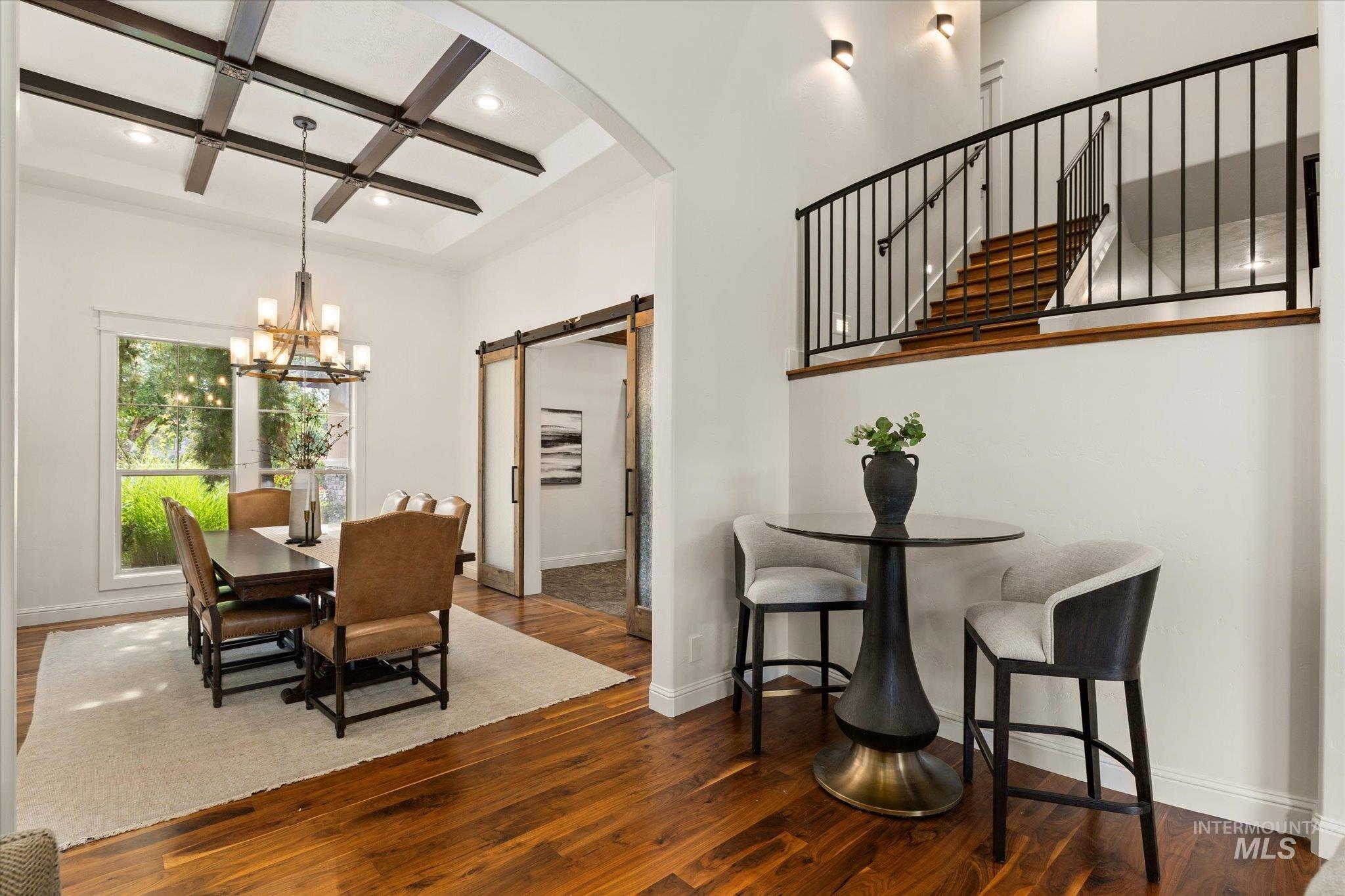 Dining space with a barn door, coffered ceiling, a chandelier, beamed ceiling, and dark wood-style flooring