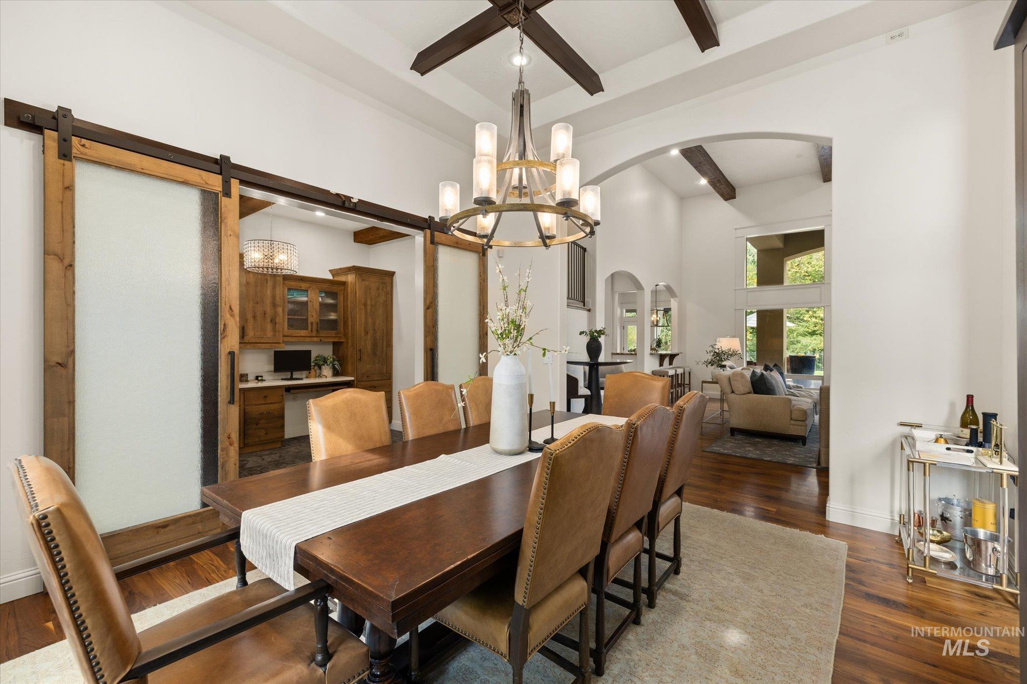 Dining room featuring beam ceiling, a chandelier, dark wood finished floors, a towering ceiling, and arched walkways