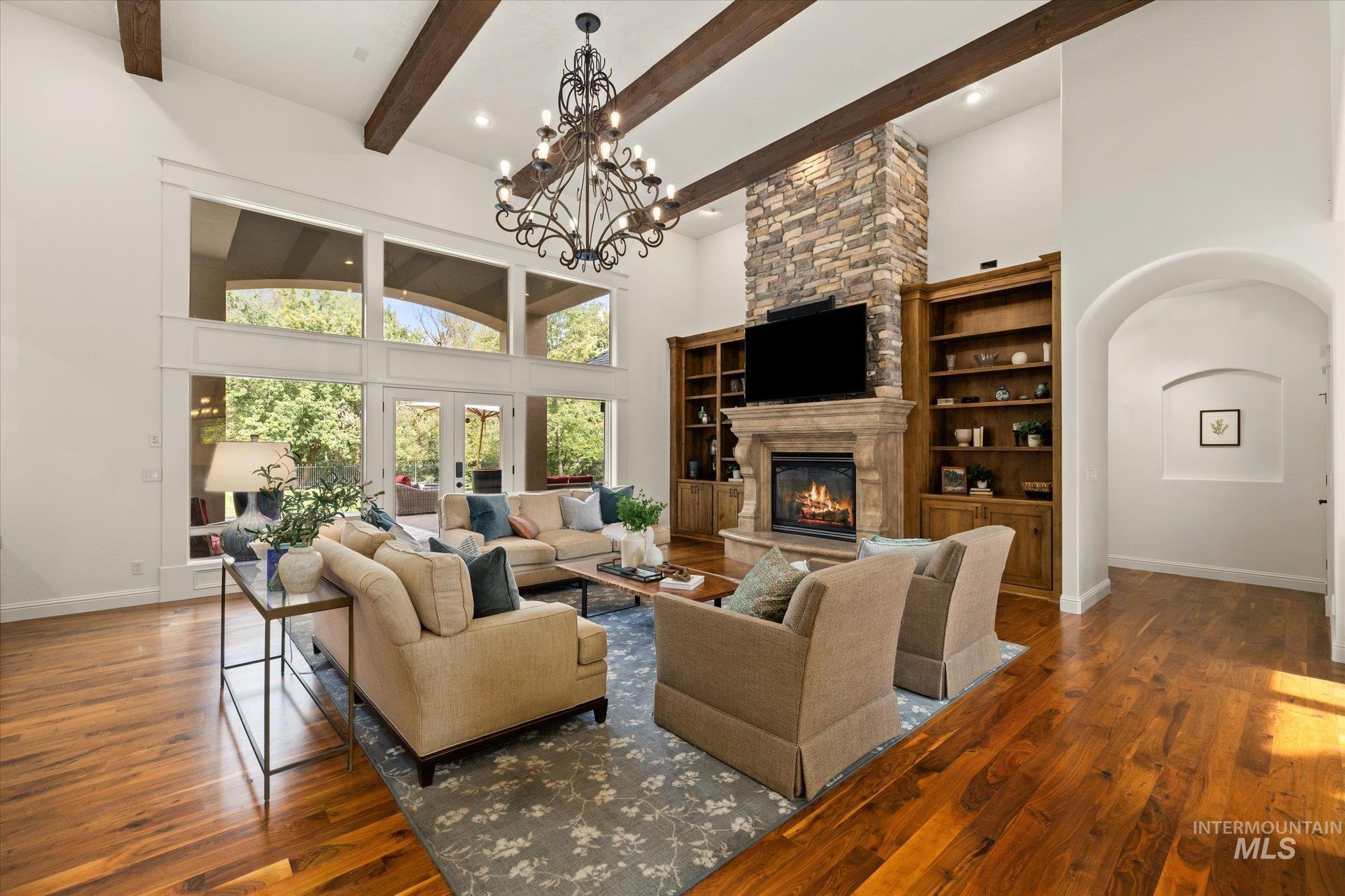 Living room featuring a towering ceiling, dark wood finished floors, a fireplace, arched walkways, and beamed ceiling