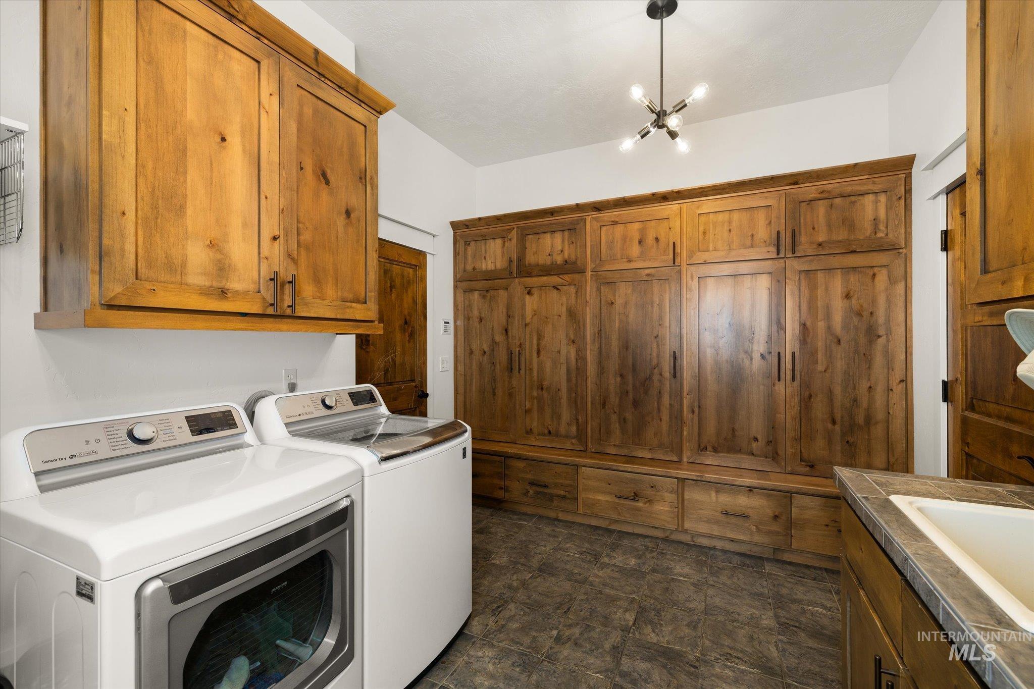 Laundry area with cabinet space, washer and clothes dryer, a chandelier, and dark stone finish flooring