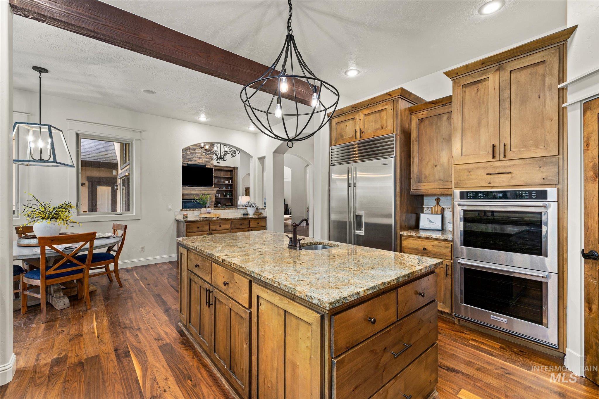 Kitchen featuring brown cabinets, dark wood-type flooring, light stone counters, recessed lighting, and beamed ceiling