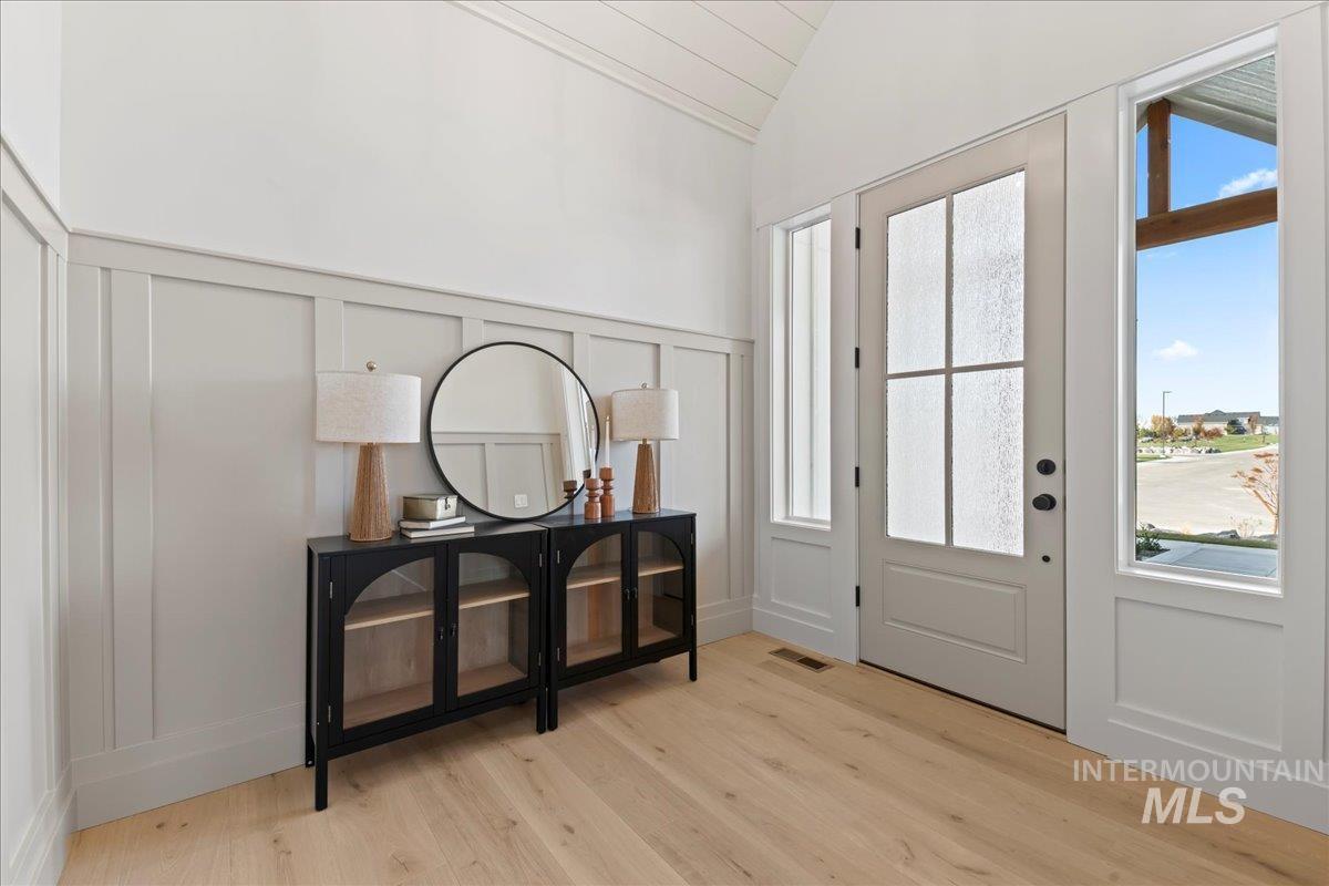 Entrance foyer featuring a decorative wall, vaulted ceiling, light wood-style floors, and a wainscoted wall