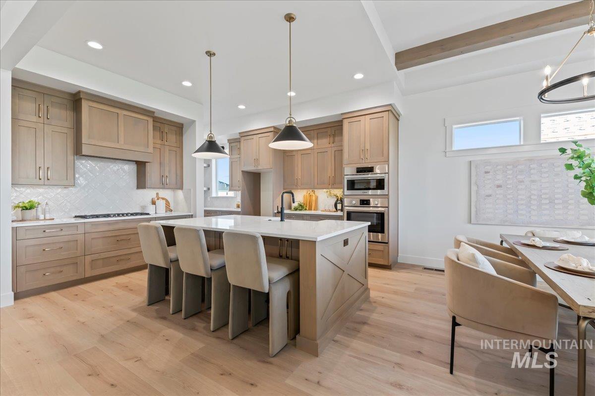 Kitchen featuring decorative light fixtures, tasteful backsplash, light stone countertops, light wood-type flooring, and beam ceiling