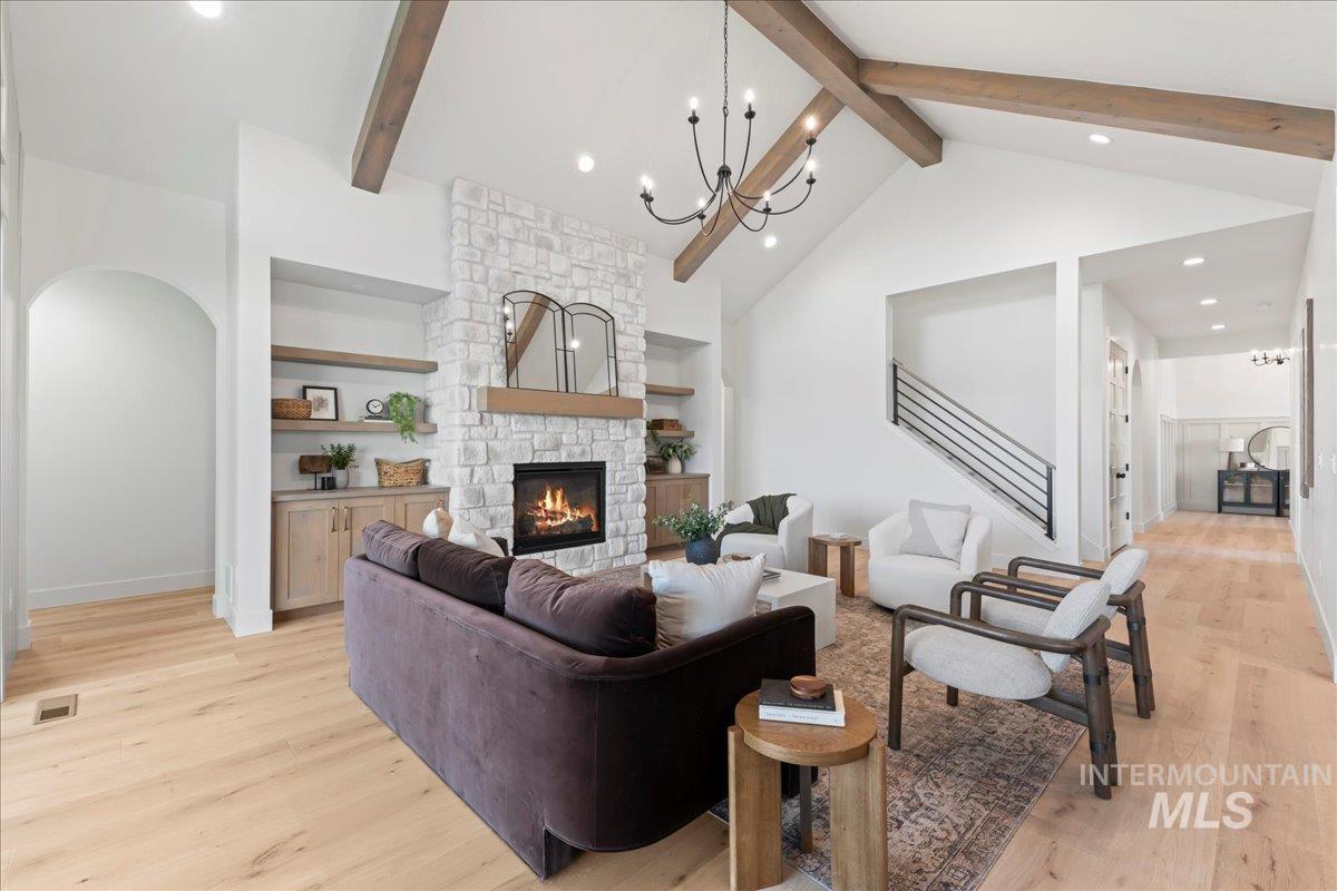 Living room with beamed ceiling, light wood-type flooring, a chandelier, recessed lighting, and a stone fireplace
