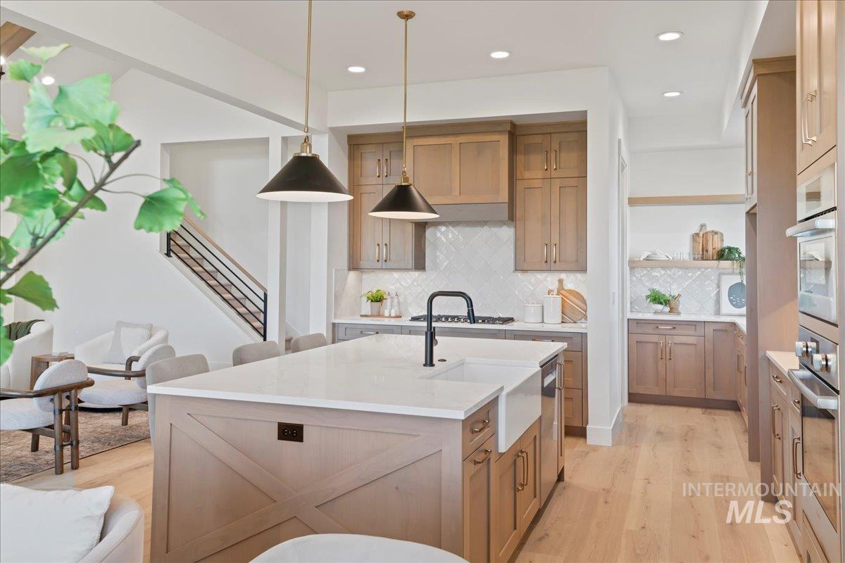 Kitchen with decorative backsplash, brown cabinetry, light wood finished floors, an island with sink, and light stone counters