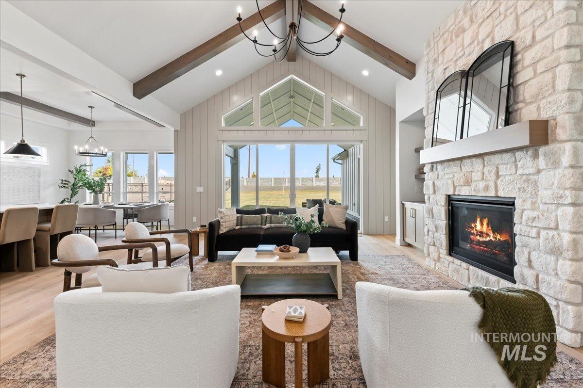 Living room with a chandelier, beamed ceiling, a stone fireplace, wood finished floors, and plenty of natural light