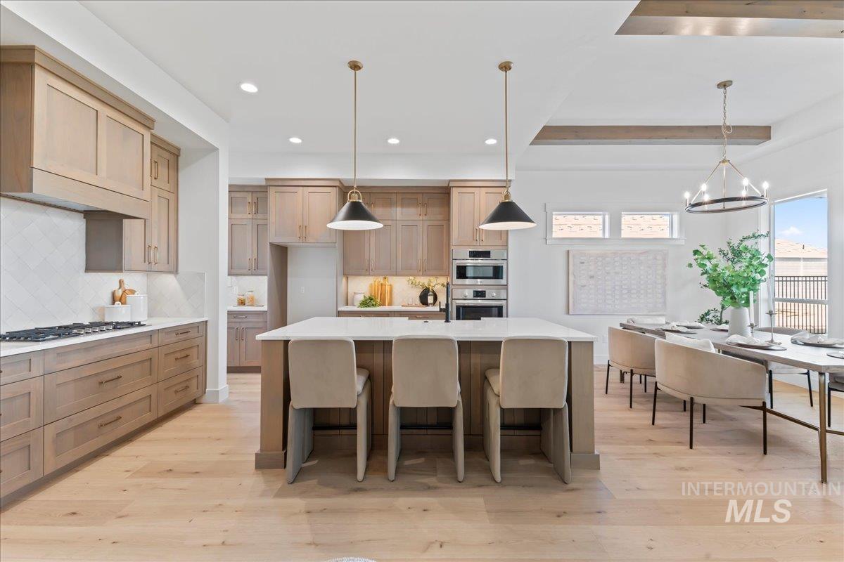 Kitchen with hanging light fixtures, backsplash, light wood-type flooring, light stone counters, and a breakfast bar