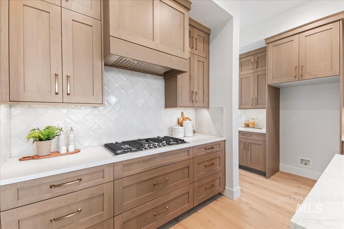 Kitchen featuring tasteful backsplash, light wood-style flooring, light stone countertops, stainless steel gas cooktop, and custom exhaust hood