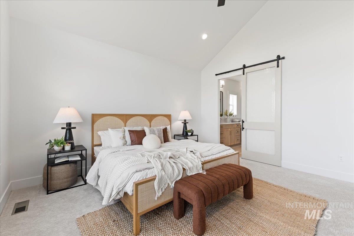 Bedroom with carpet flooring, a barn door, high vaulted ceiling, ensuite bath, and ceiling fan
