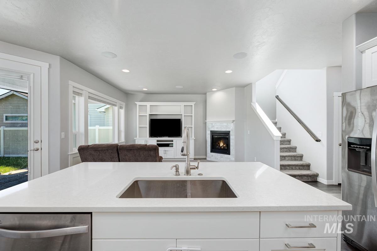 Kitchen featuring appliances with stainless steel finishes, a glass covered fireplace, open floor plan, white cabinetry, and recessed lighting