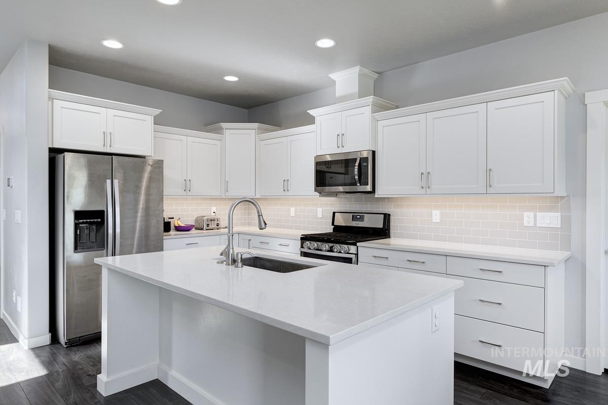 Kitchen with stainless steel appliances, backsplash, recessed lighting, and white cabinets